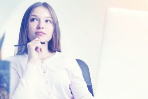 xAPI Authoring Tools can be cause for concern. You need to choose carefully. Closeup of thoughtful young woman with pencil in hand sitting at desk with laptop and office tools. Toned image