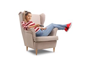 Young woman seated in an armchair watching TV isolated on white background